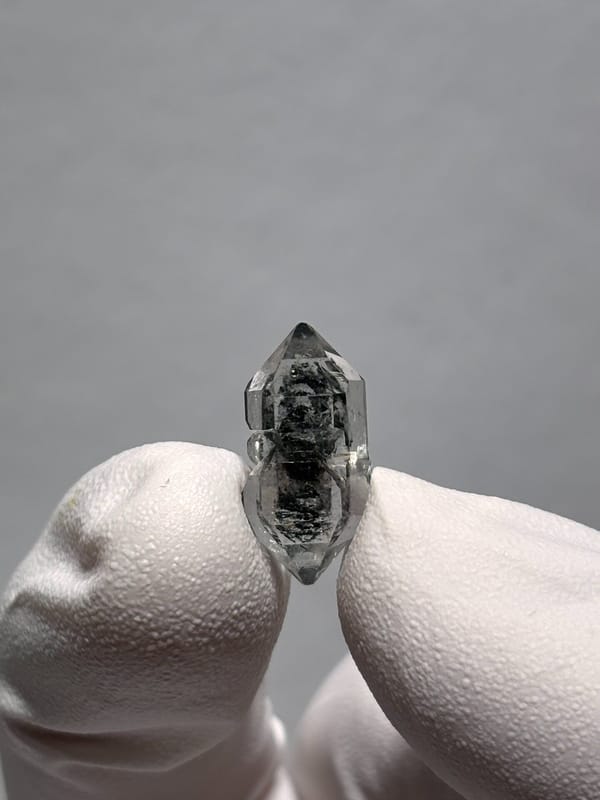 Very tiny black sugar-core double-terminated quartz from Yunnan, China, held in gloved hand