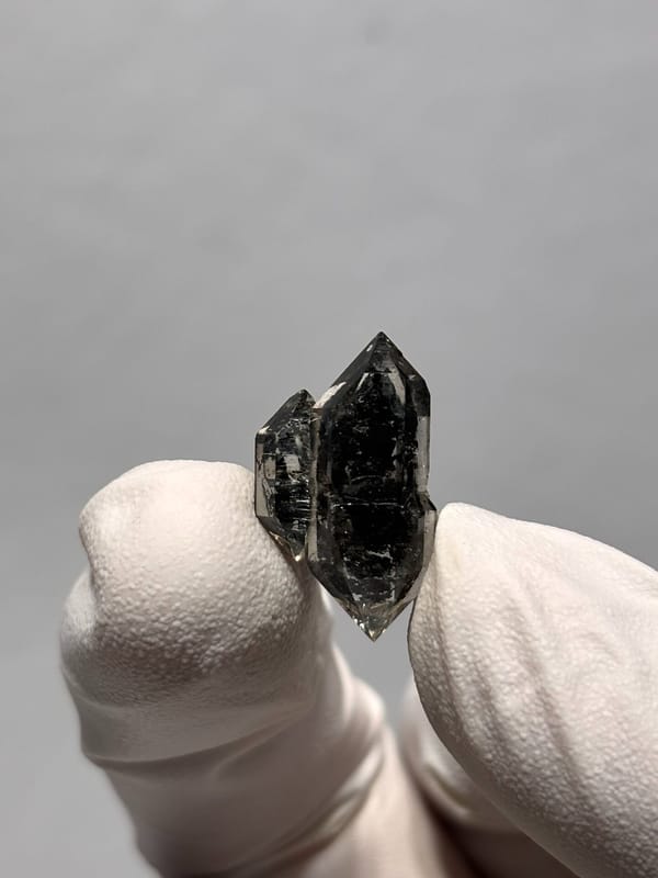 Tiny black sugar-core quartz with side crystal from Yunnan, China, held in gloved hand