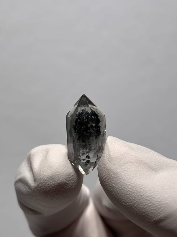 Tiny black sugar-core double-terminated quartz from Yunnan, China, held in gloved hand