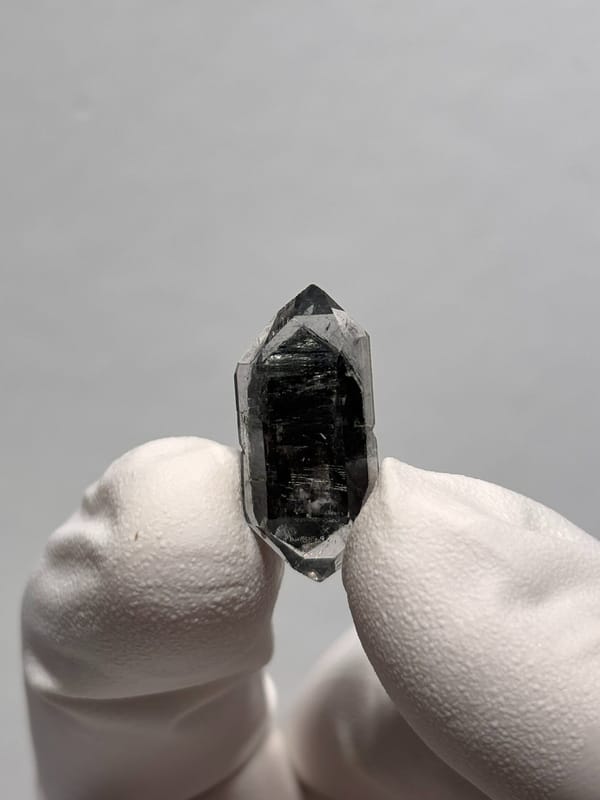 Tiny black sugar-core double-terminated quartz from Yunnan, China, held in gloved hand