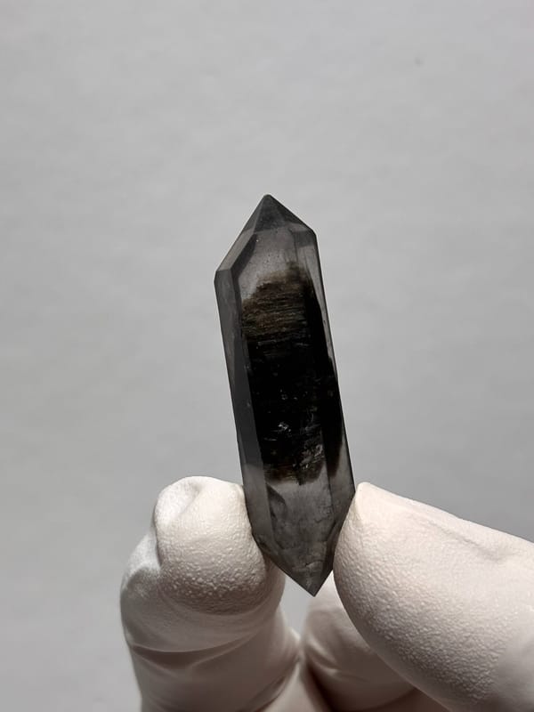 Slender black sugar-core double-terminated quartz from Yunnan, China, held in gloved hand