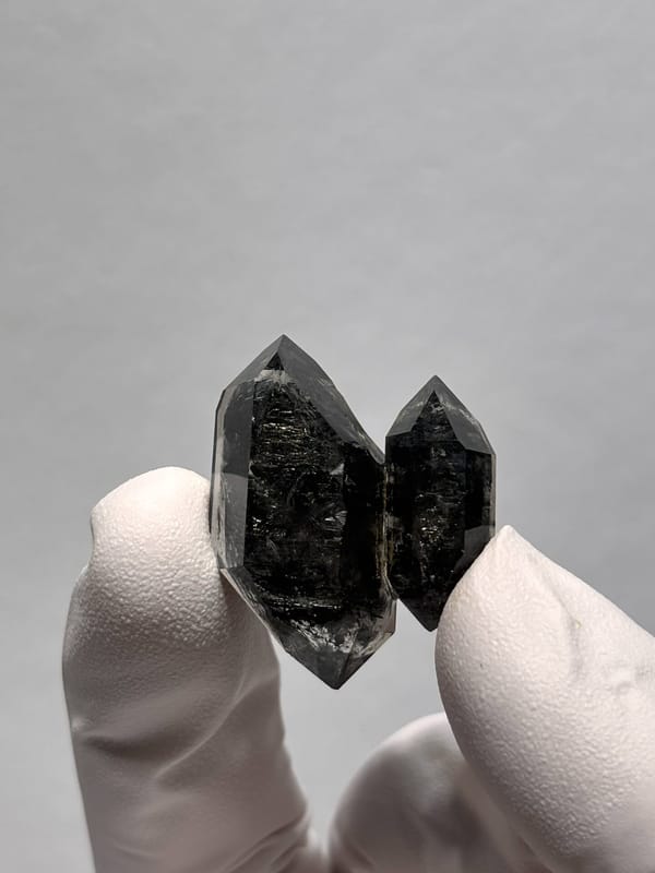 Twinned black double-terminated quartz pair from Yunnan, China, held in gloved hand