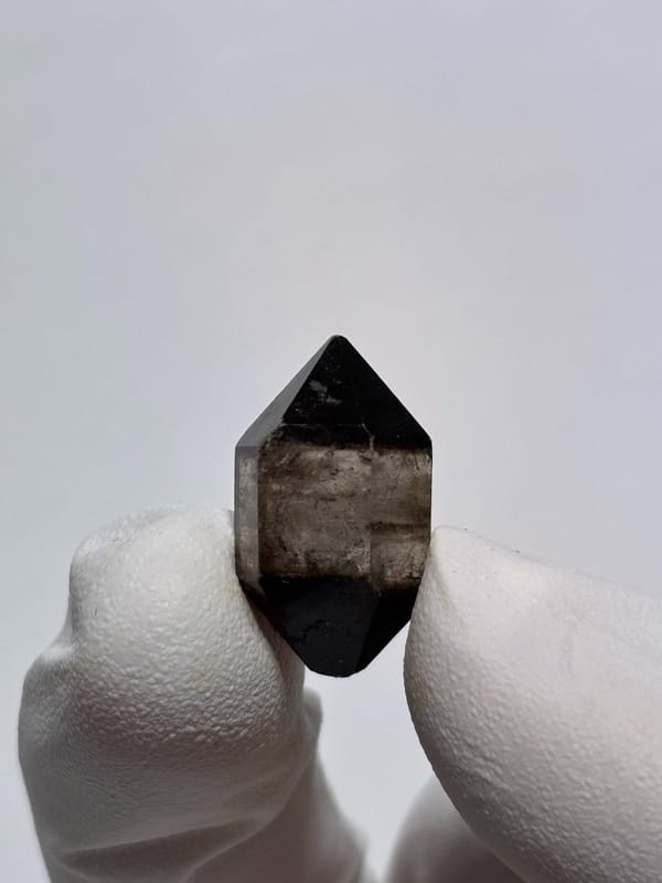 Tiny black-capped double-terminated quartz from Yunnan, China, held on gloved fingertip