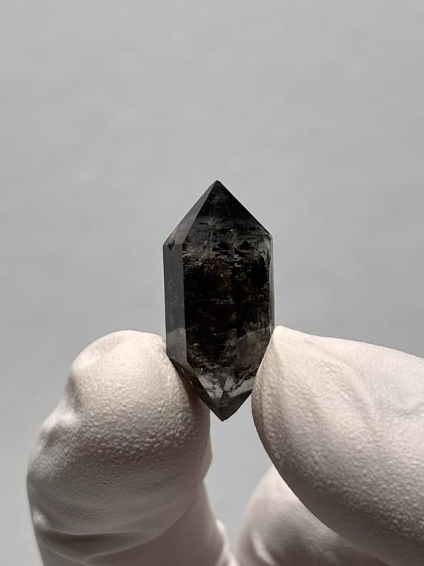 Tiny black-flecked double-terminated quartz from Yunnan, China, held in gloved hand