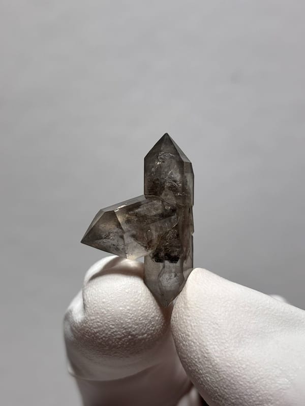 Tiny black-flecked quartz pair with crossing crystal from Yunnan, China, held in gloved hand