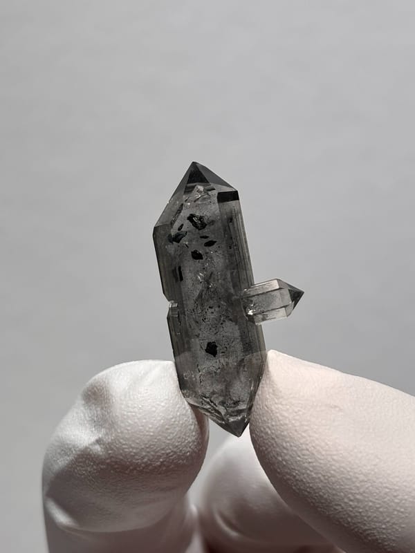 Black-flecked double-terminated quartz with side crystal from Yunnan, China, held in gloved hand