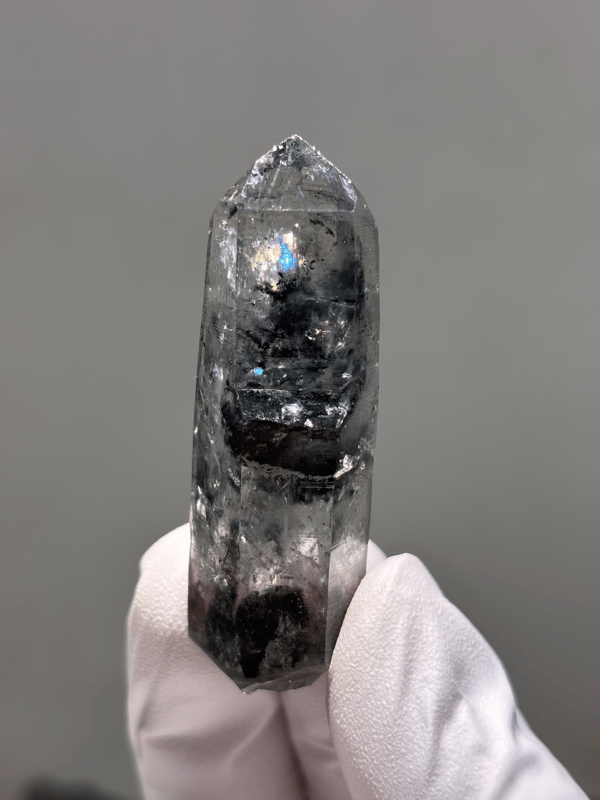 Black-included quartz point with rainbow flash from Jinkouhe, Sichuan, China, held in gloved hand
