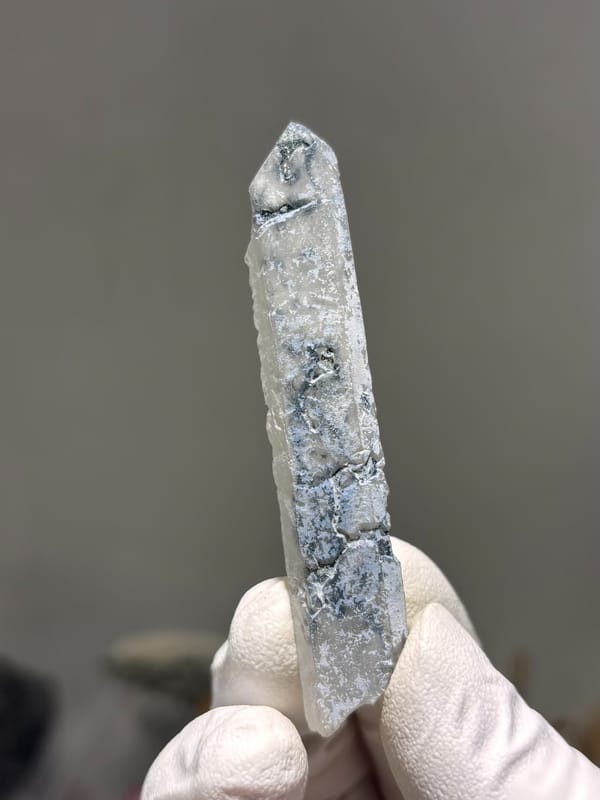 Slender blue-grey quartz wand with complete tip from Inner Mongolia, China, held in gloved hand