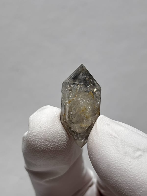 Tiny burst-crystal double-terminated quartz with golden flecks from Yunnan, China, held in gloved hand