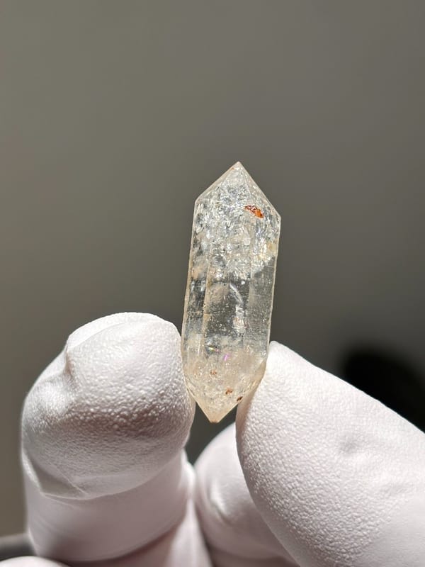 Tiny burst-crystal double-terminated quartz with golden flecks from Yunnan, China, held in gloved hand
