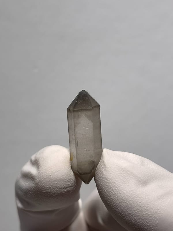 Tiny smoky capped double-terminated quartz from Yunnan, China, held in gloved hand