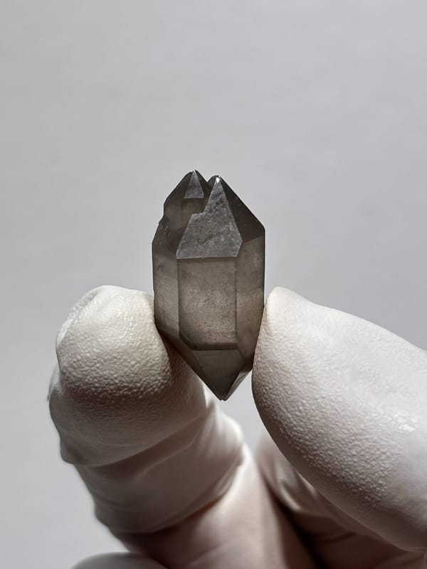 Tiny smoky capped double-terminated quartz from Yunnan, China, held in gloved hand