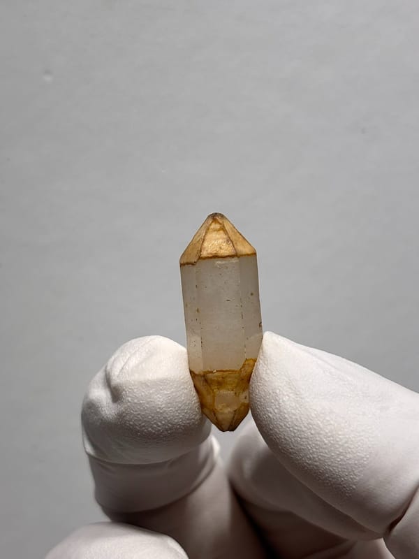 Orange-capped double-terminated quartz with flowered tips from Yunnan, China, held in gloved hand