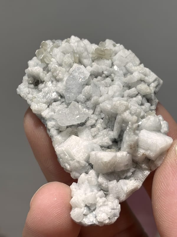 White feldspar plate with pale aquamarine and quartz from Xuebaoding, Sichuan, China, held in hand