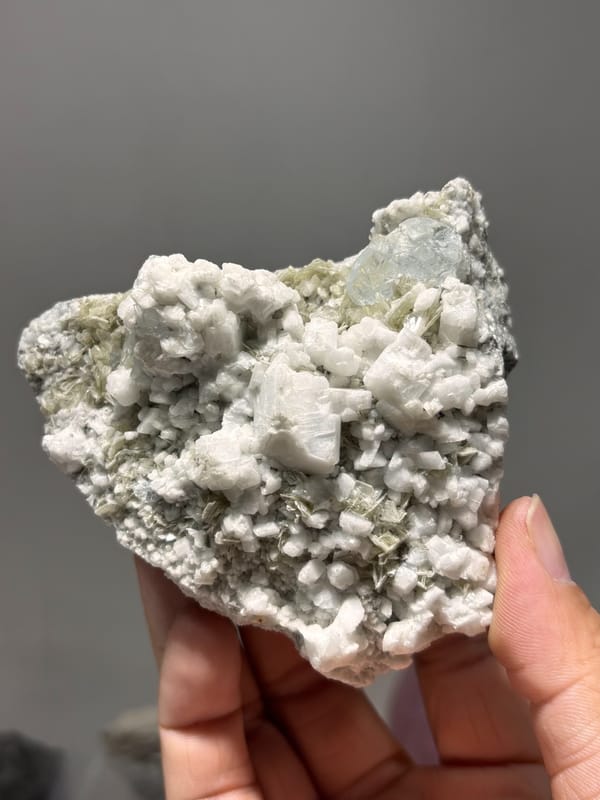 White feldspar plate with pale aquamarine crystals from Xuebaoding, Sichuan, China, held in hand