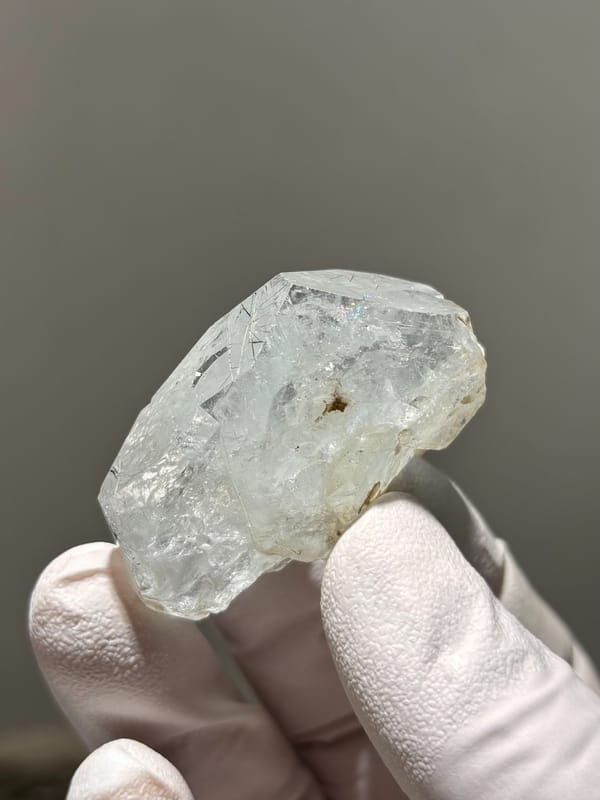 Clear aquamarine tablet with jamesonite needles inside from Xuebaoding, Sichuan, China, held in gloved hand