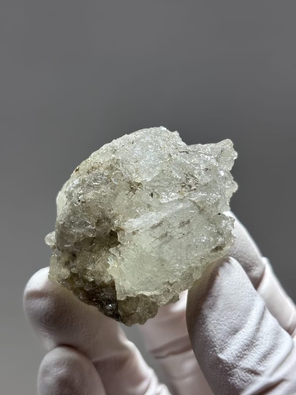 Etched aquamarine with mica and feldspar from Sichuan, China, held in gloved hand