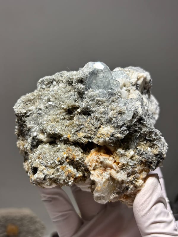 Aquamarine plate with mica and feldspar from Xuebaoding, Sichuan, China, held in gloved hand