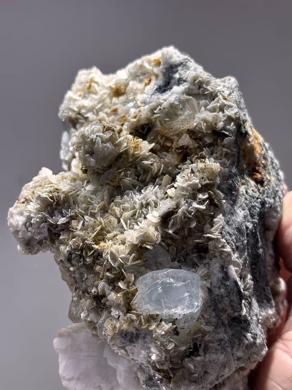Dark mica block with aquamarine, cassiterite and scheelite from Xuebaoding, Sichuan, China, held in hand