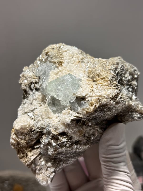 Free-standing mica block with pale blue aquamarine from Xuebaoding, Sichuan, China, held in gloved hand