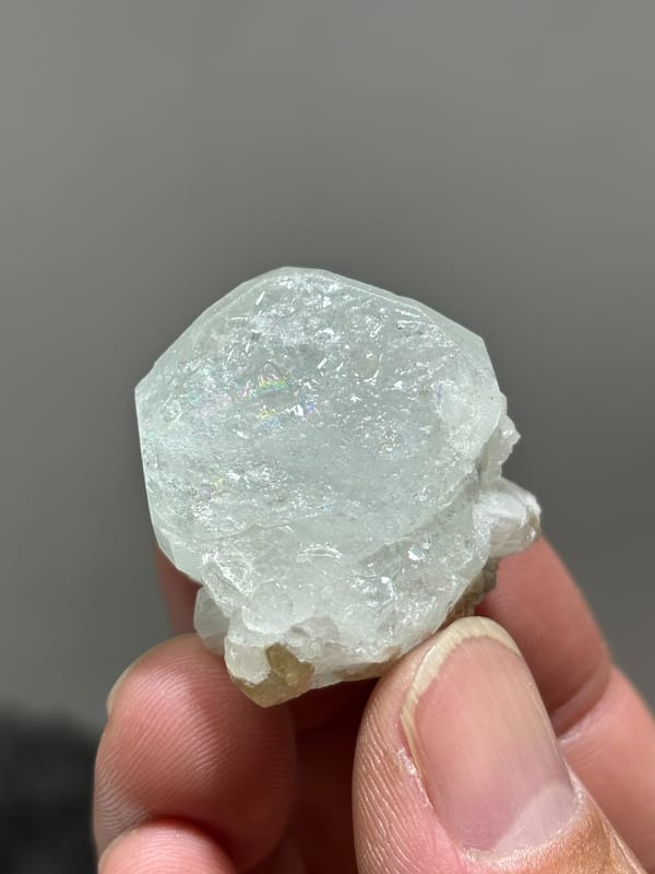 Glassy pale aquamarine with iridescent faces and scheelite from Xuebaoding, Sichuan, China, held in hand