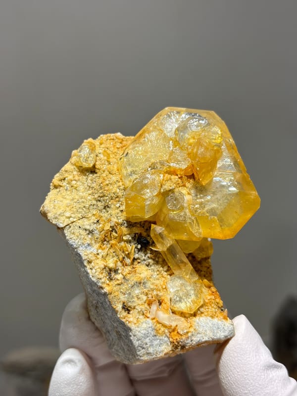 Golden-stained aquamarine with quartz, mica and cassiterite from Xuebaoding, Sichuan, China, held in gloved hand