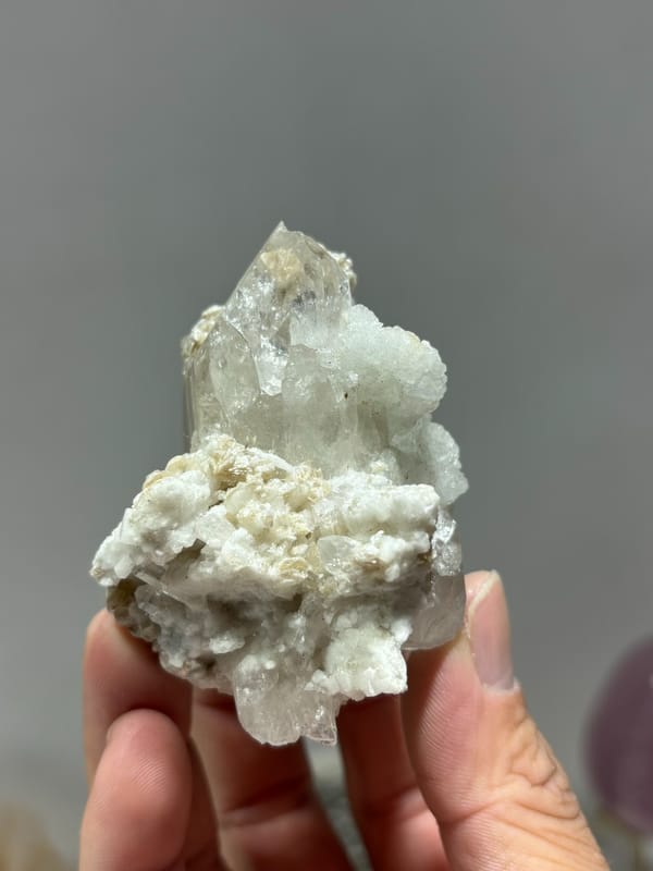 Quartz point over white feldspar with aquamarine and mica from Xuebaoding, Sichuan, China, held in hand