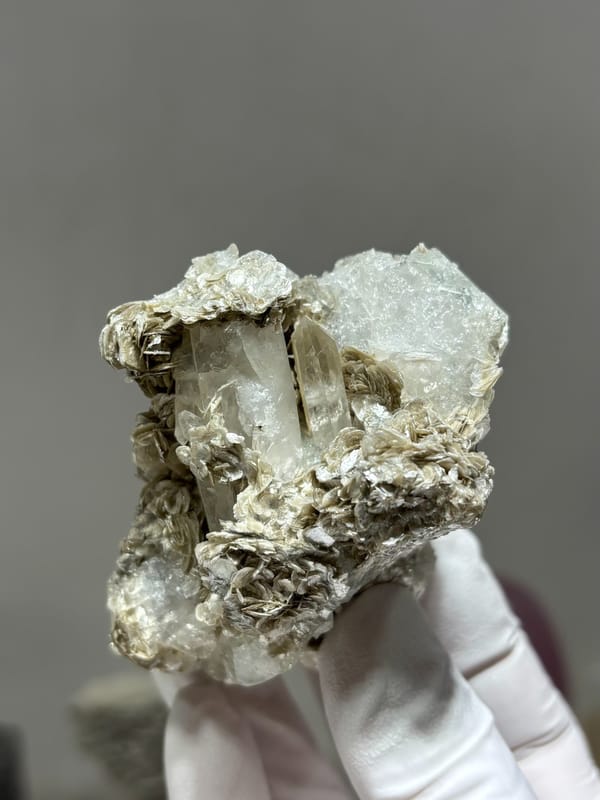 Clear quartz prism with pale aquamarine and mica from Xuebaoding, Sichuan, China, held in gloved hand