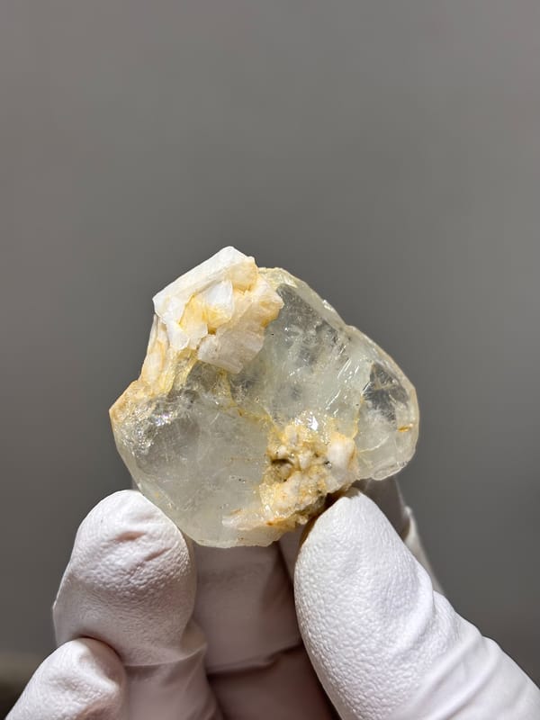 Clear aquamarine with golden feldspar patches from Xuebaoding, Sichuan, China, held in gloved hand