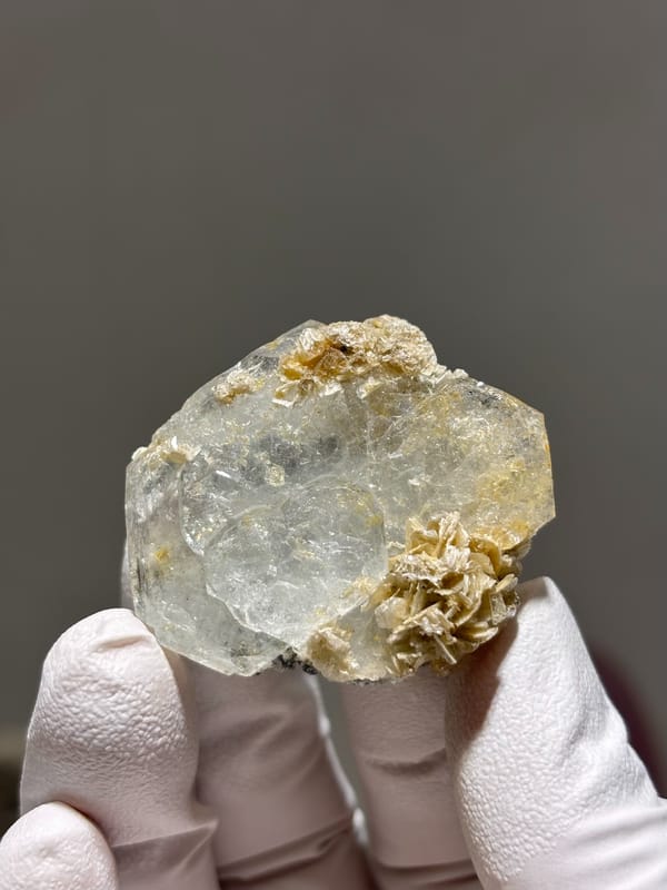 Clear aquamarine tablet with mica and jamesonite from Xuebaoding, Sichuan, China, held in gloved hand