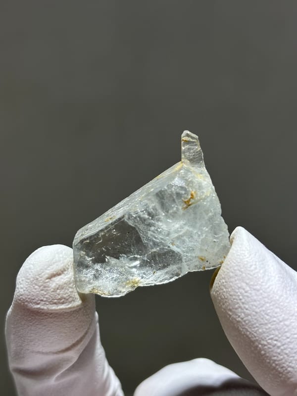 Tiny clear aquamarine crystal from Xuebaoding, Sichuan, China, held in gloved hand