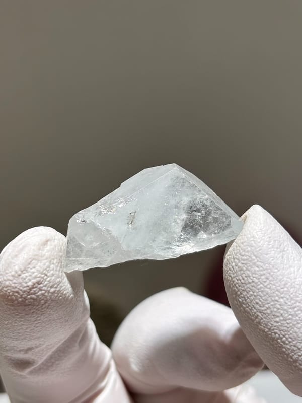 Tiny clear aquamarine tablet from Xuebaoding, Sichuan, China, held in gloved hand