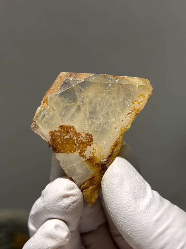 Clear aquamarine tablet with golden patch from Xuebaoding, Sichuan, China, held in gloved hand
