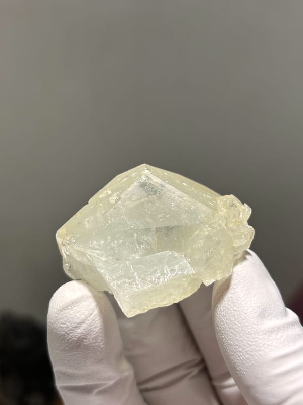 Complete pale yellow aquamarine floater from Xuebaoding, Sichuan, China, held in gloved hand