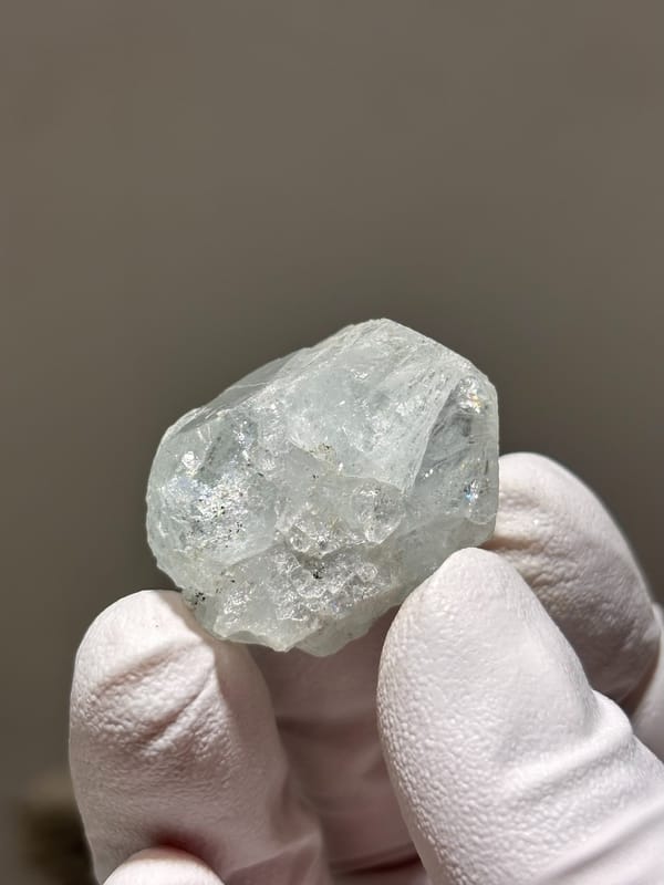 Frosted pale green aquamarine nugget from Xuebaoding, Sichuan, China, held in gloved hand