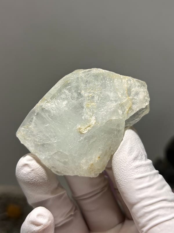Frosted pale green aquamarine tablet from Xuebaoding, Sichuan, China, held in gloved hand