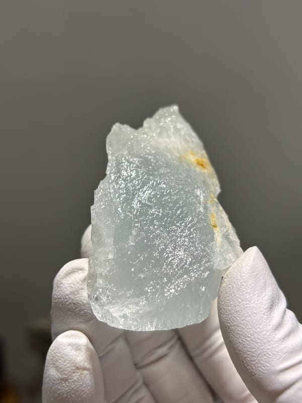 Frosted pale green aquamarine prism from Xuebaoding, Sichuan, China, held in gloved hand