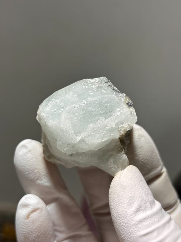 Frosted pale green aquamarine block from Xuebaoding, Sichuan, China, held in gloved hand