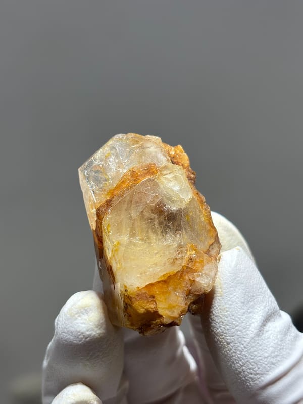 Gel-flower aquamarine with orange skin from Sichuan, China, held in gloved hand