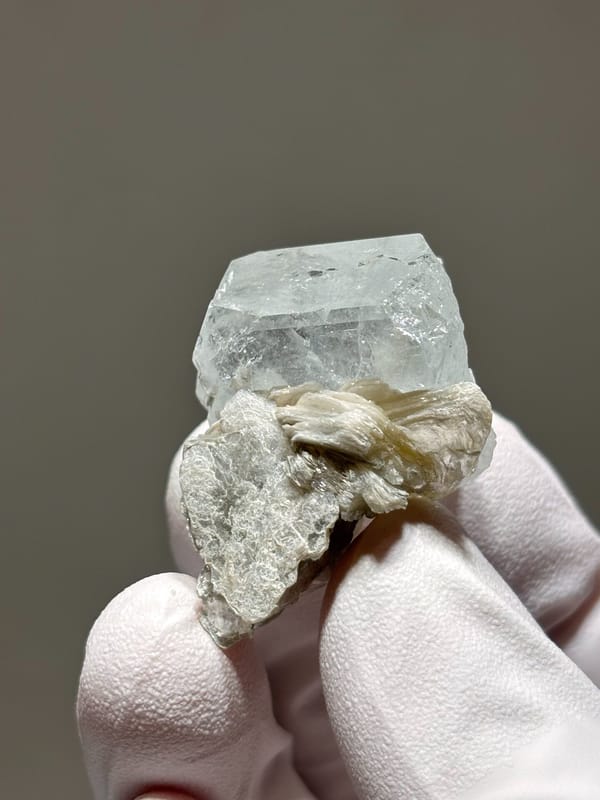 Glassy aquamarine with mica rosette from Xuebaoding, Sichuan, China, held in gloved hand