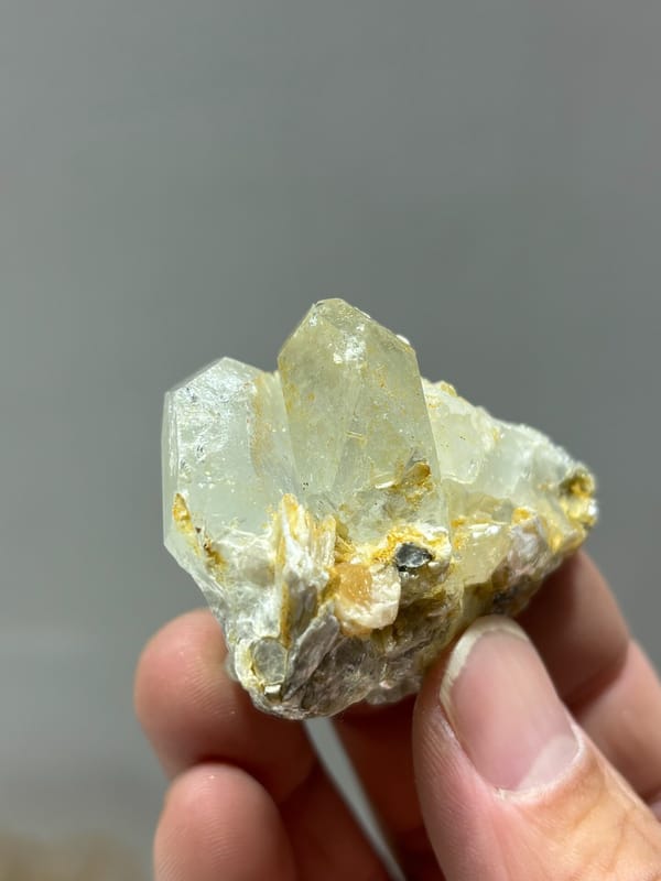 Glassy aquamarine group with mica and scheelite from Xuebaoding, Sichuan, China, held in hand
