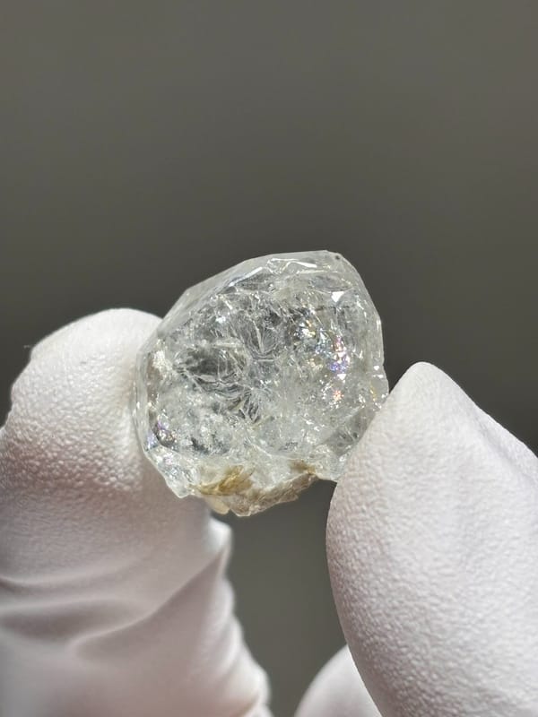 Tiny glassy aquamarine crystal from Xuebaoding, Sichuan, China, held in gloved hand