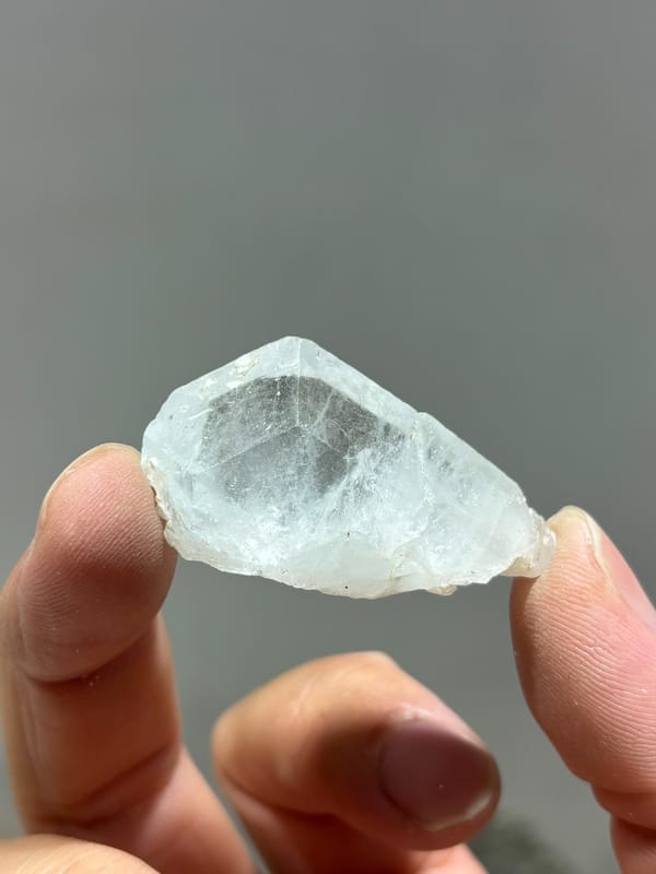 Glassy pale blue aquamarine floater tablet from Xuebaoding, Sichuan, China, held in hand