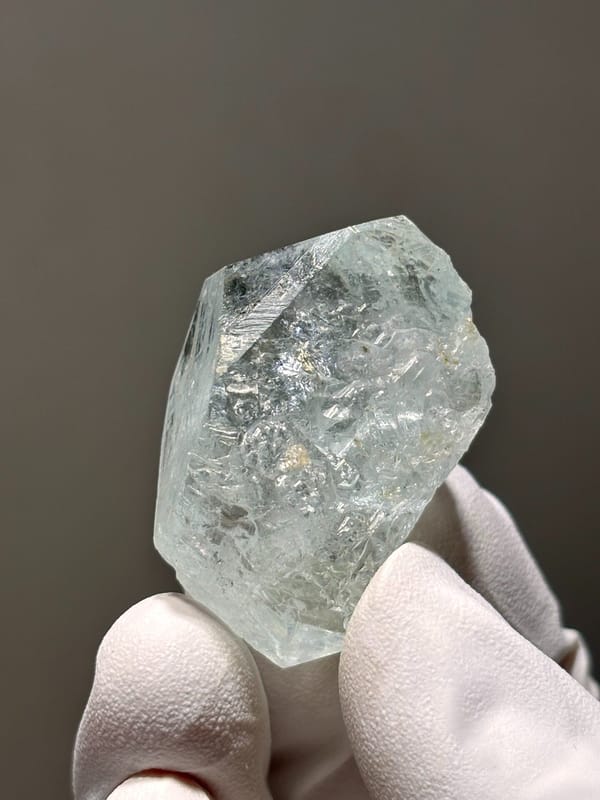 Glassy pale blue aquamarine crystal from Xuebaoding, Sichuan, China, held in gloved hand