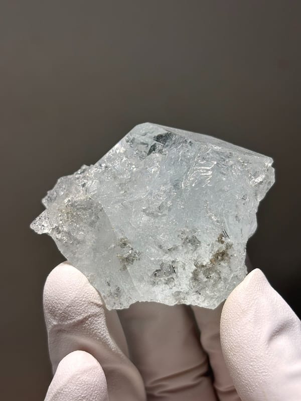 Glassy pale blue aquamarine block from Xuebaoding, Sichuan, China, held in gloved hand