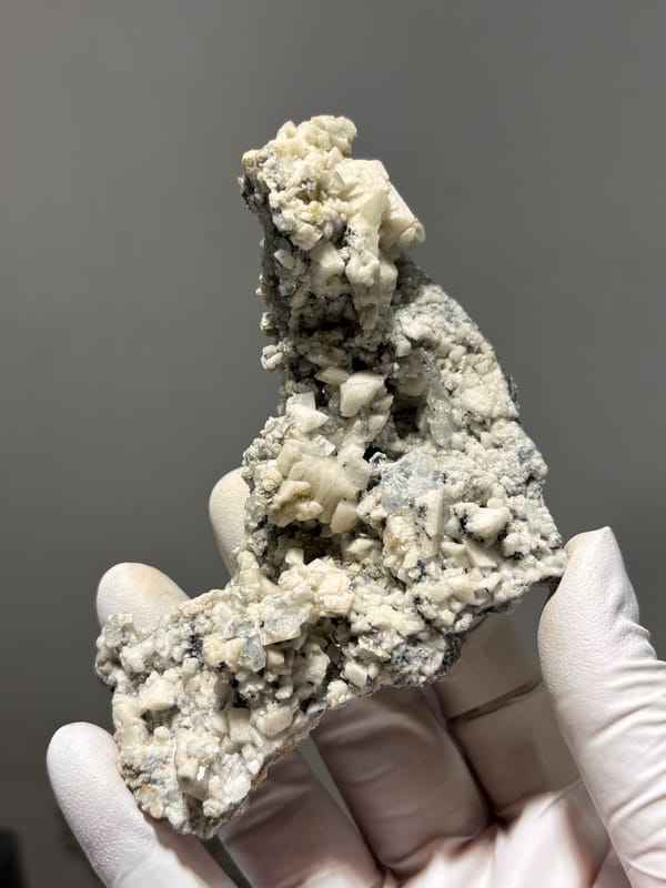 Grey matrix spire with aquamarine, mica and feldspar from Xuebaoding, Sichuan, China, held in gloved hand