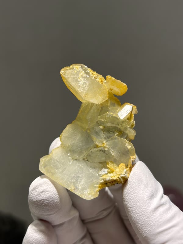 Multi-crystal aquamarine group with golden mica from Xuebaoding, Sichuan, China, held in gloved hand