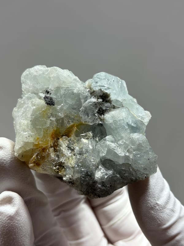 Multi-crystal aquamarine group with golden patch from Xuebaoding, Sichuan, China, held in gloved hand