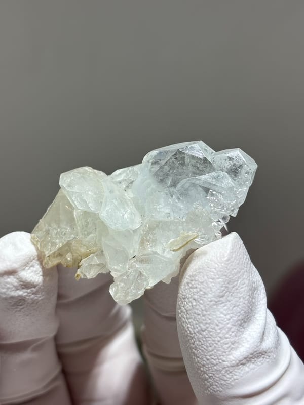 Multi-crystal clear aquamarine group from Xuebaoding, Sichuan, China, held in gloved hand