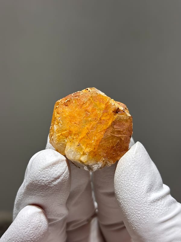 Orange-stained aquamarine tablet from Xuebaoding, Sichuan, China, held in gloved hand